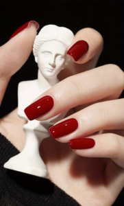 vernis semi-permanent pailleté reflechissant avec ongles rouge et statuette dans la main avec fond noir